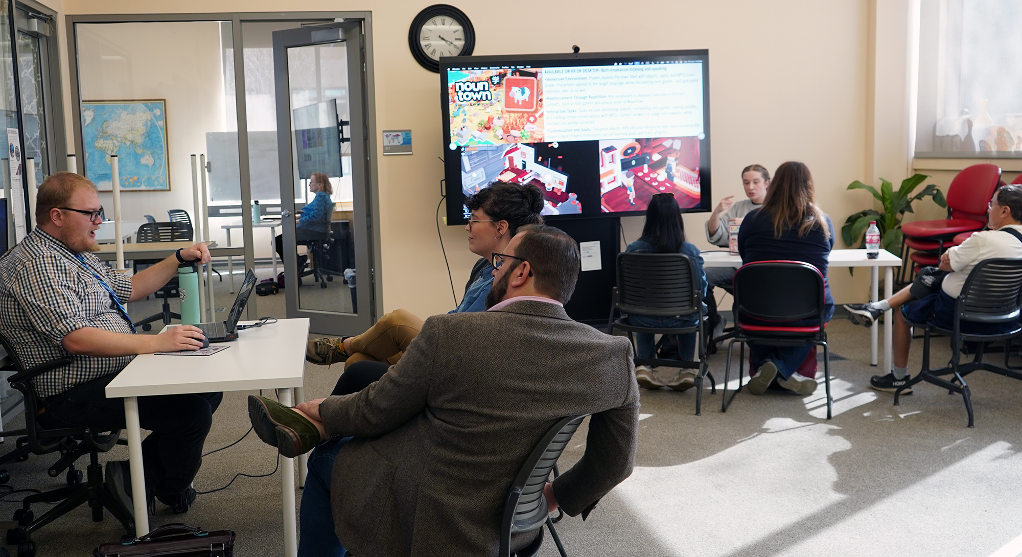 The Innovative Pedagoy Expo held on March 19, 2026. Three stations of the innovative pedagogy expo. Left: Michael Hall, presenting on "Videogames Belong in the Classroom"; back right, Jenna Allemand presenting "NounTown for Language Learning"; back center, Kathy Comfort presenting "Creating a Medical Case Study in French." Not pictured: Maria Comsa, who presented "NotebookLM for Multimodal Language Learning." The event took place in the WLDH Studio on March 19, 2026.